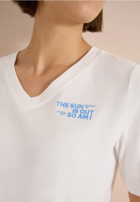 Weißes V-Neck-Shirt mit blauem Schriftzug „THE SUN IS OUT GO AMT“ auf der Brust.