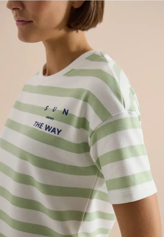Vrouw draagt een wit-groen gestreept T-shirt met de tekst 'SUN THE WAY'.