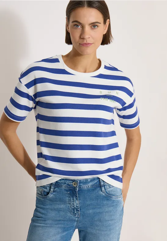 Persoon draagt wit-blauw gestreept T-shirt en spijkerbroek voor een lichte achtergrond.