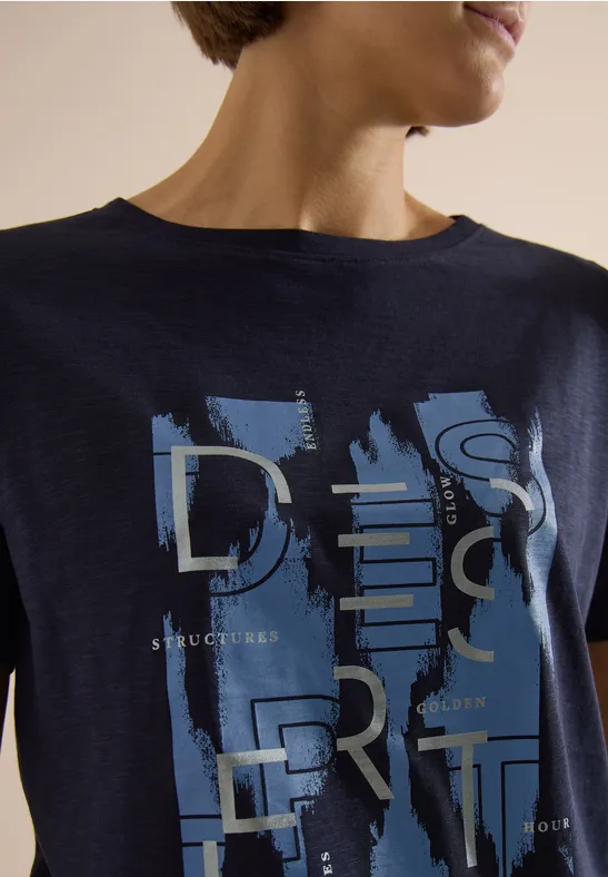 Dunkelblaues T-Shirt mit abstrakten Pinselstrichen und silbernen Lettern am Oberkörper.