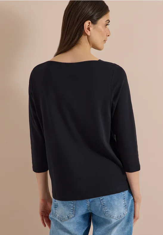 Frau von hinten, trägt schwarzes 3/4-Ärmelshirt und blaue Jeans.