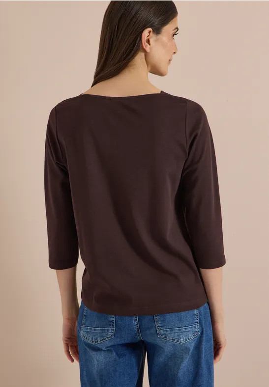 Femme de dos en tee-shirt marron à manches trois-quarts et jean sur fond beige.