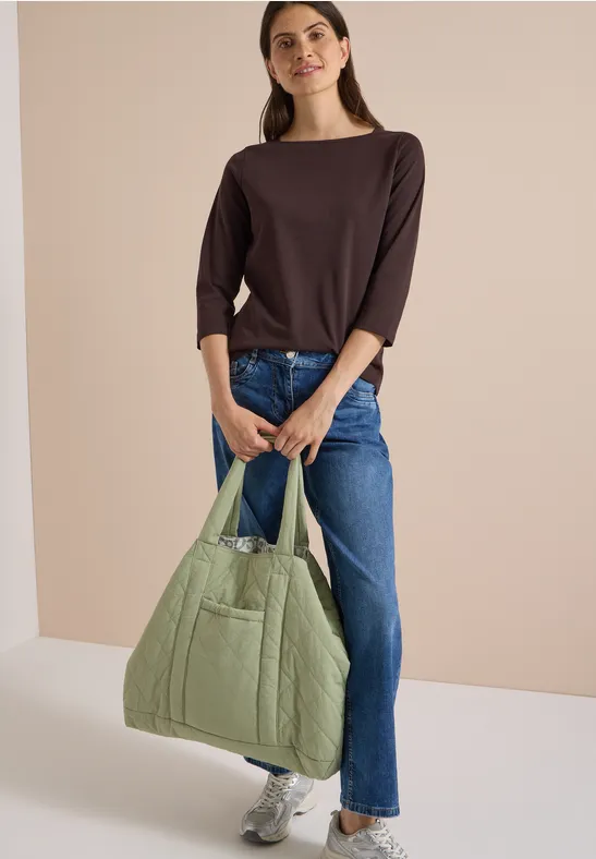 Femme en haut marron et jean porte un grand sac matelassé vert clair et des baskets blanches.