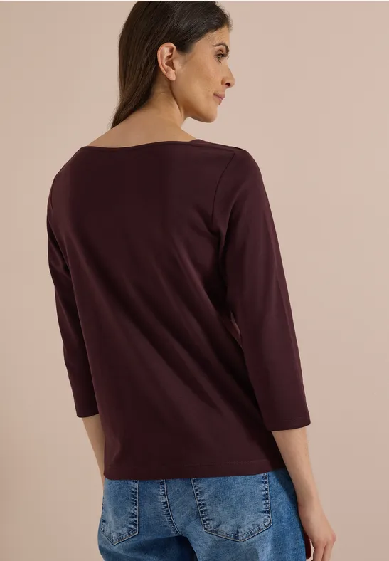 Frau in weinrotem Dreiviertelarmshirt, Rückansicht, blaue Jeans