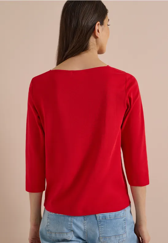Frau von hinten in rotem Dreiviertelarm-Shirt und blauer Jeans