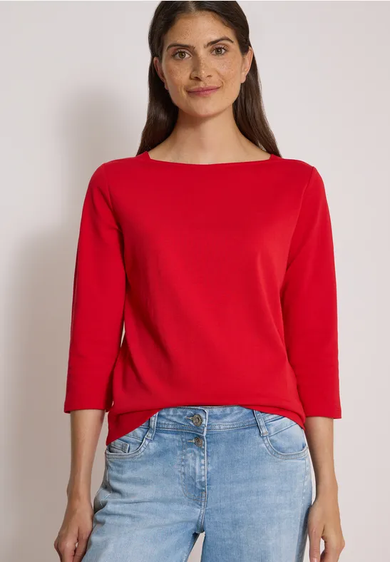 Frau in rotem Dreiviertelärmel-Shirt und Jeans vor hellem Hintergrund