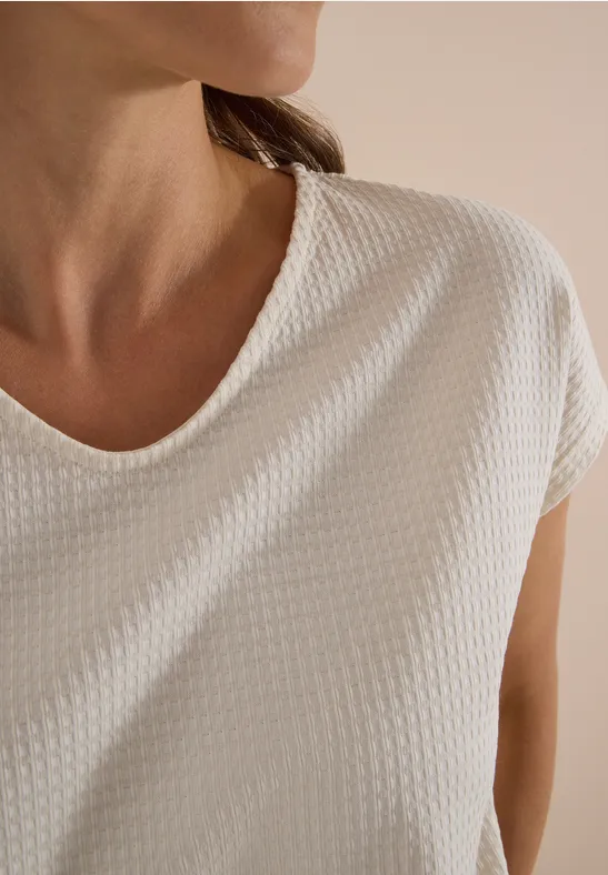 Oberkörper einer Person im strukturierten weißen T-Shirt, nur Hals und Schultern sichtbar.