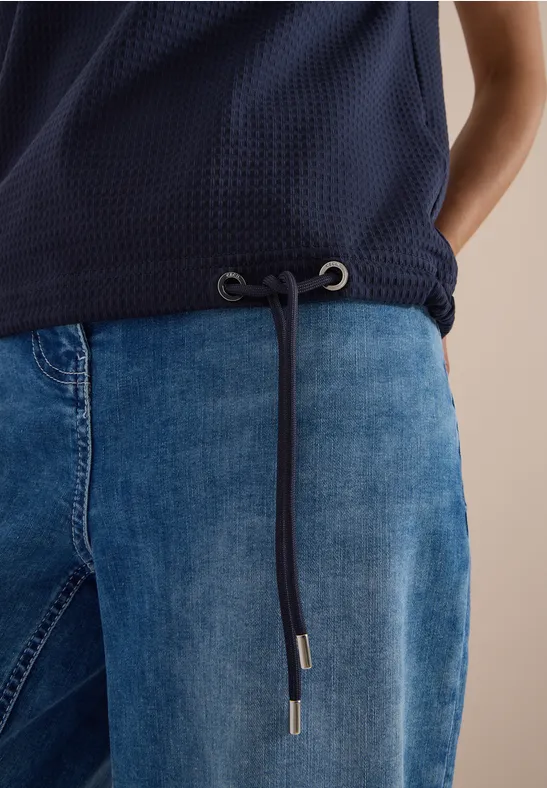 Nahaufnahme einer dunkelblauen Bluse mit Kordelzug und blauer Jeanshose.