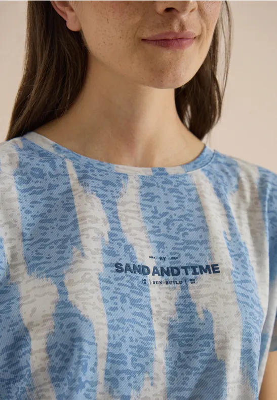 Portrait d'une femme portant un t-shirt rayé bleu et blanc avec l'inscription 'SAND AND TIME'