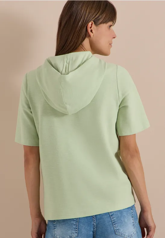 Vrouw van achteren in lichtgroene korte mouw hoodie en blauwe spijkerbroek.