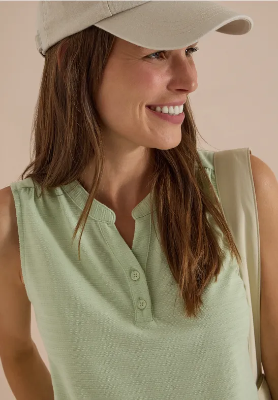 Jeune femme souriante en débardeur vert clair à boutons et casquette beige.
