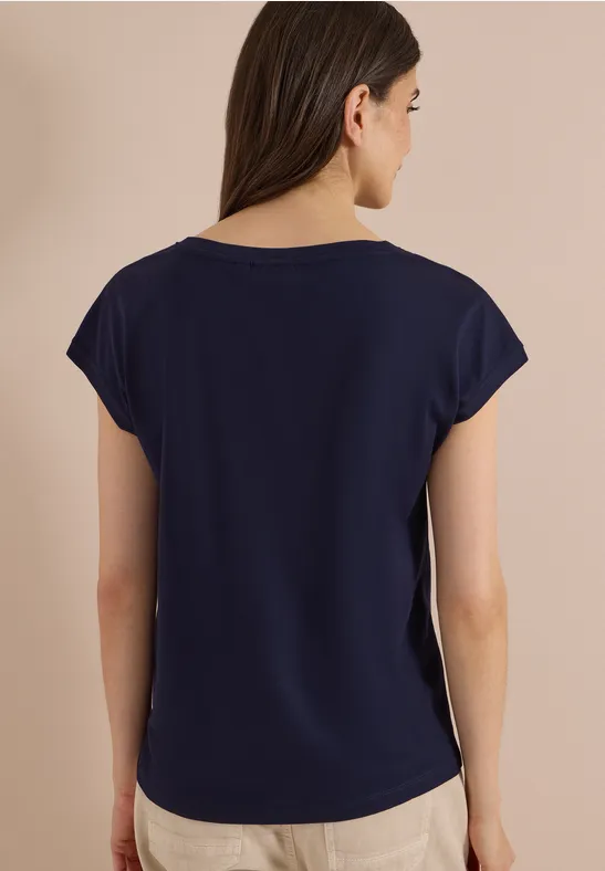 Rückansicht einer Frau in dunkelblauem T-Shirt vor beigem Hintergrund.
