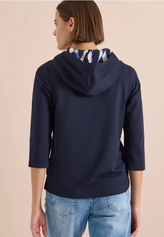 Rückansicht einer Frau in dunkelblauem Hoodie mit 3/4-Ärmeln und Jeans.