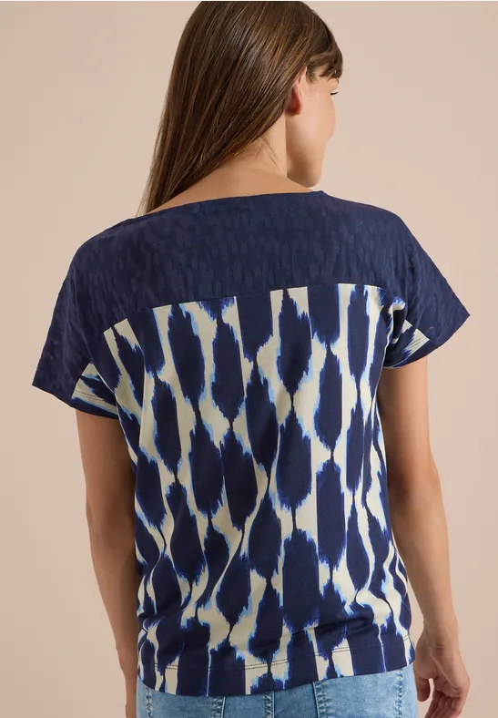 Frau von hinten in blau-weiß gemustertem, locker sitzendem Shirt mit kurzen Ärmeln.