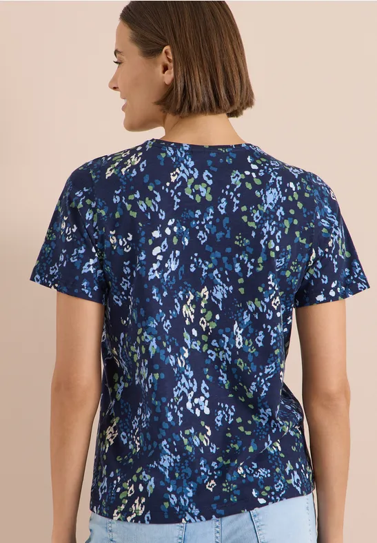 Eine Frau von hinten trägt eine dunkelblaue, kurzärmelige Bluse mit kleinem, buntem Blumenmuster.