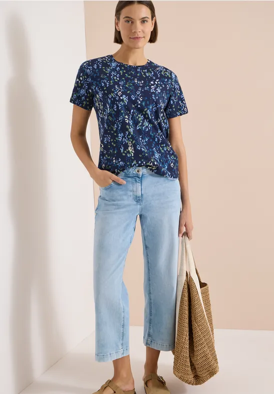 Frau in marineblauem Blumen-T-Shirt, hellen, weit geschnittenen Jeans und mit großer Korbtasche.