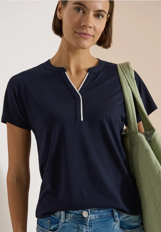 Frau in marineblauem T-Shirt mit kurzem Reißverschluss am Ausschnitt, trägt grüne Stofftasche.