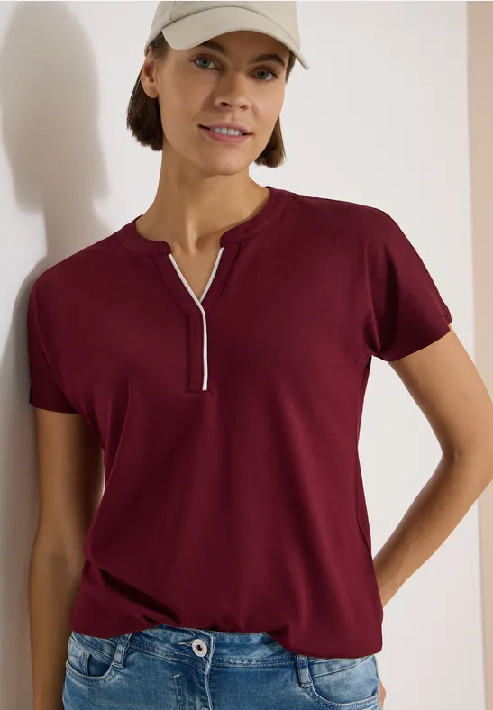 Person trägt bordeauxrotes T-Shirt mit Reißverschlussschlitz am Ausschnitt und Jeans