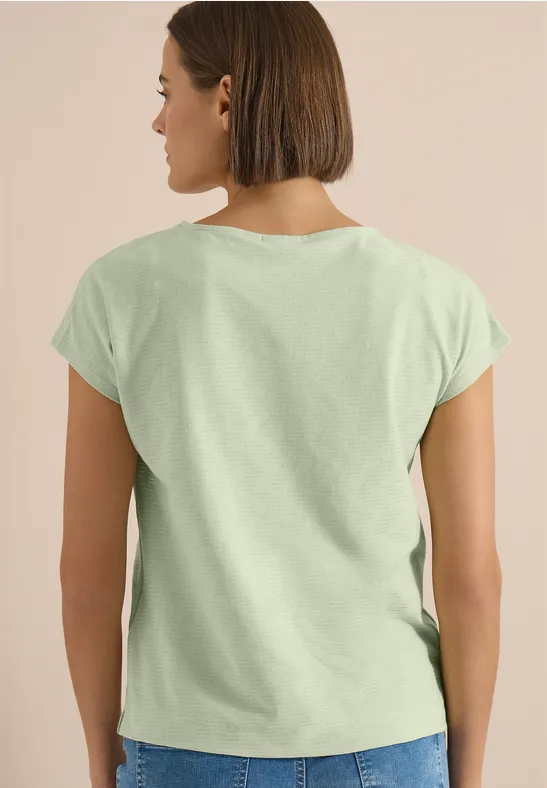 Frau von hinten in einem hellgrünen T-Shirt vor neutralem Hintergrund mit schulterlangem Bob.