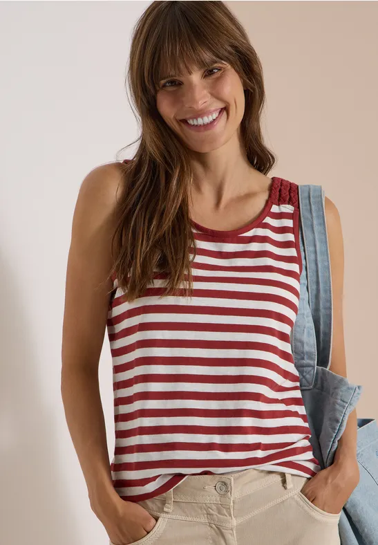 Fröhliche Frau im rot-weiß gestreiften Tanktop, trägt eine Jeansjacke lässig über der Schulter.