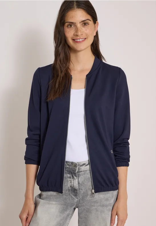 Femme en blouson aviateur bleu marine sur débardeur blanc et jean gris, style décontracté chic.