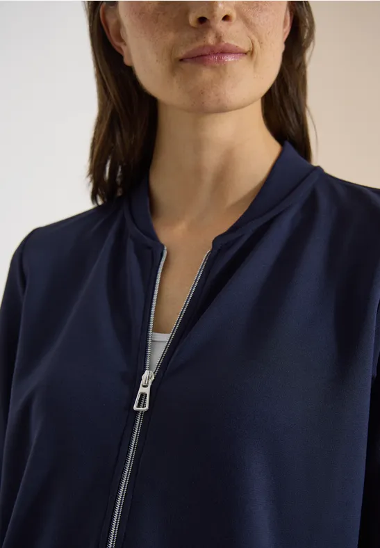 Femme portant une veste bleu foncé à zip partiellement ouvert, avec la tirette argentée visible.