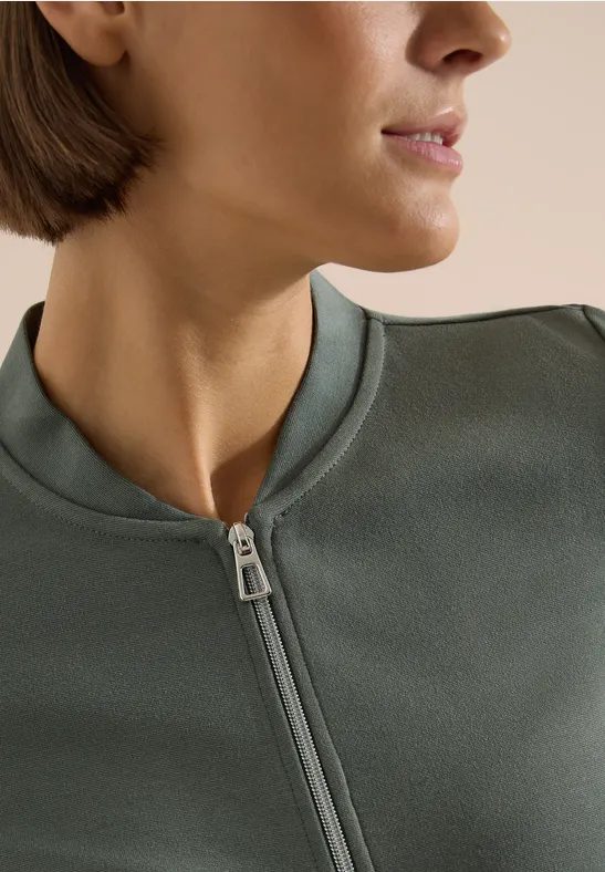 Nahaufnahme einer seitlichen Ansicht einer Person in einem olivgrünen, hochgeschlossenen Reißverschluss-Pullover.