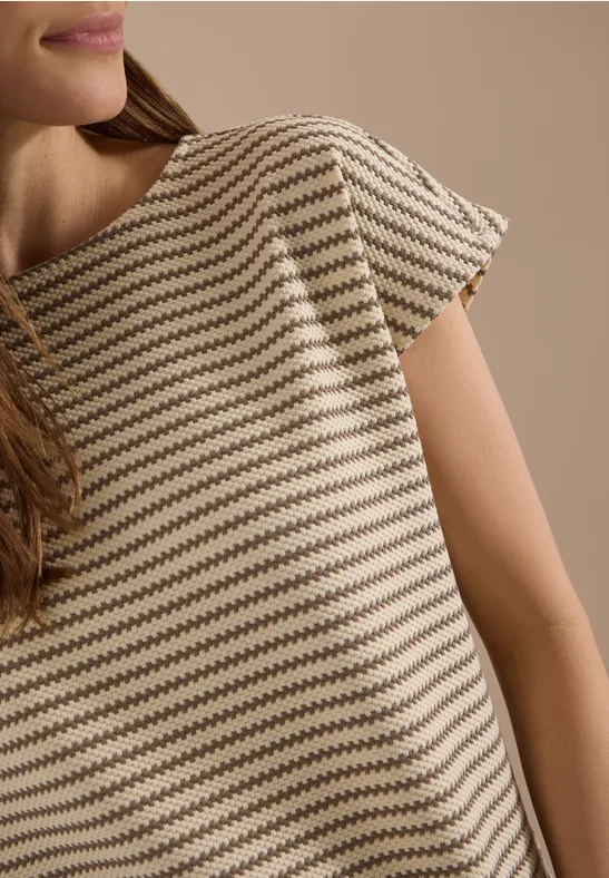Close-up van een vrouw in een beige T-shirt met korte mouwen en bruine strepen voor een neutrale achtergrond.