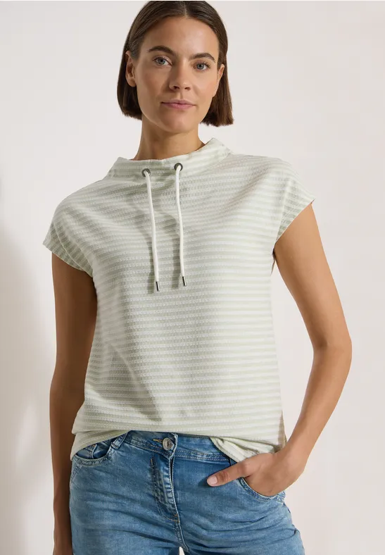 Femme portant un t-shirt à capuche manches courtes rayé avec cordon et un jean sur fond neutre.