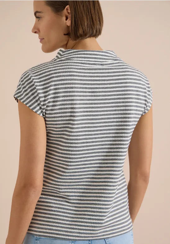 Vrouw van achteren in een gestreept T-shirt tegen neutrale achtergrond.