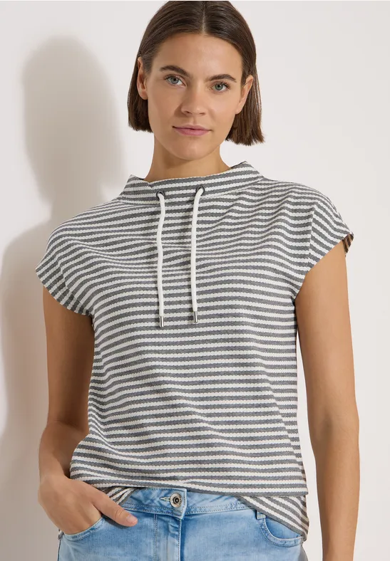 Vrouw in gestreept, kort mouwig hoodie-T-shirt met capuchon, handen in de zakken.