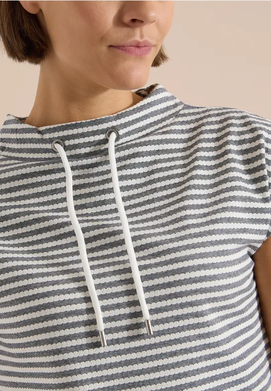 Vrouw draagt een grijs-wit gestreept shirt met korte mouwen en losse koordkraag.