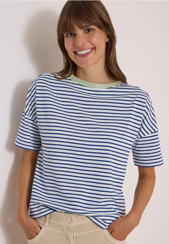 Eine lächelnde Frau in gestreiftem T-Shirt, die die Hände in die Taschen steckt.