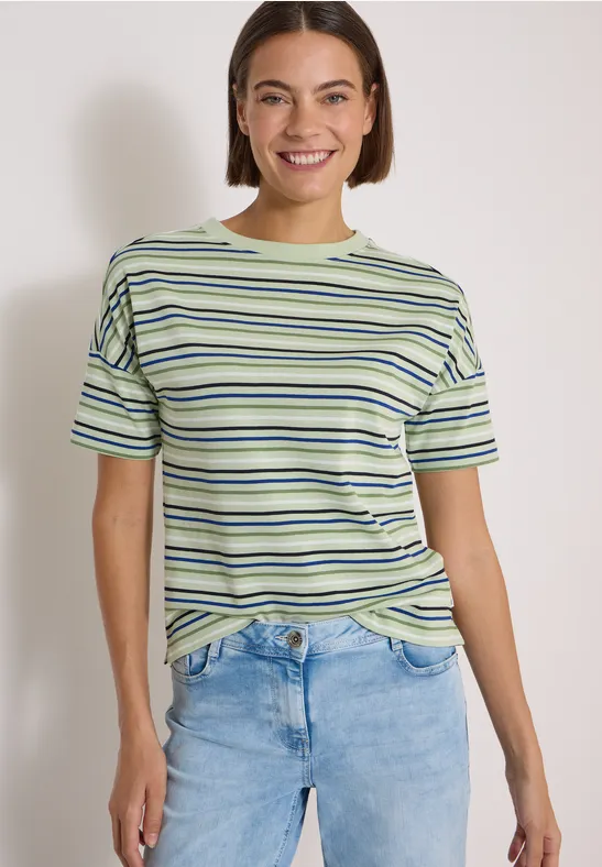 Glimlachende vrouw met gestreept T-shirt en spijkerbroek tegen lichte achtergrond.