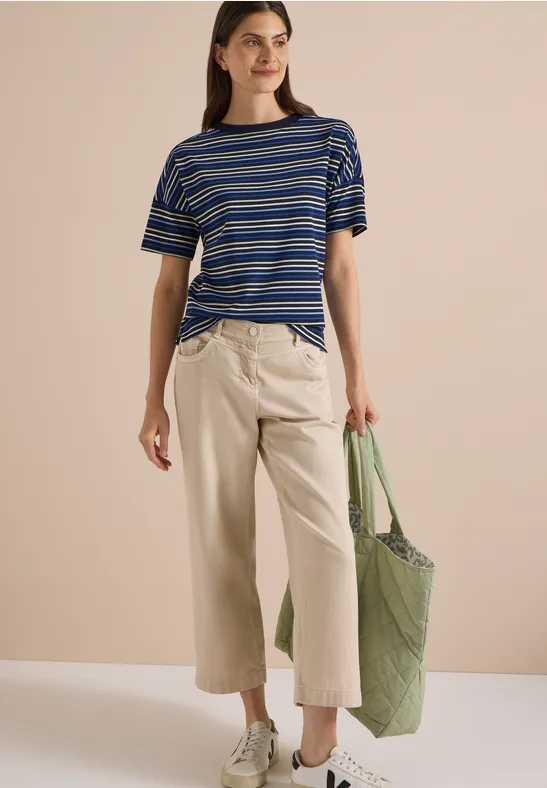 Vrouw in blauw-wit gestreept shirt, beige wijde culotte en groene schoudertas