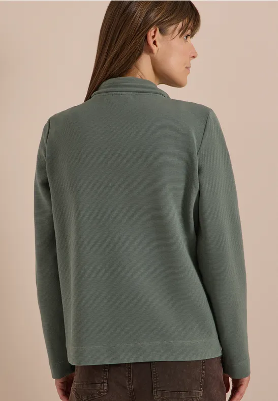 Achteraanzicht van vrouw in groene, casual blazer met een bruine broek.