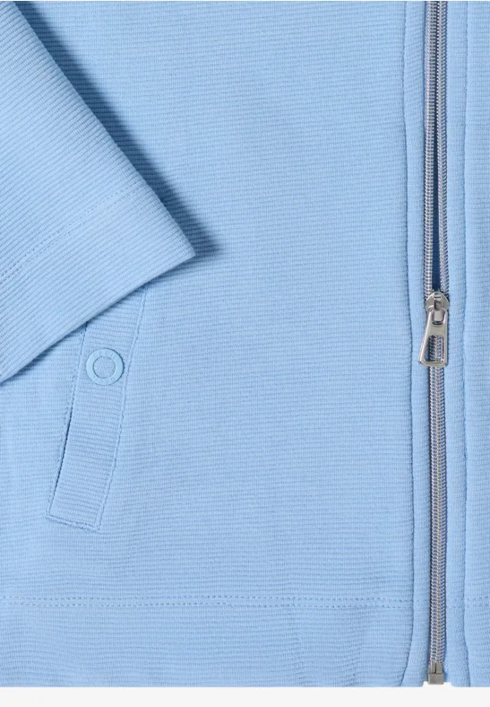 Nahaufnahme eines hellblauen Kleidungsstücks mit Reißverschluss und Druckknopf