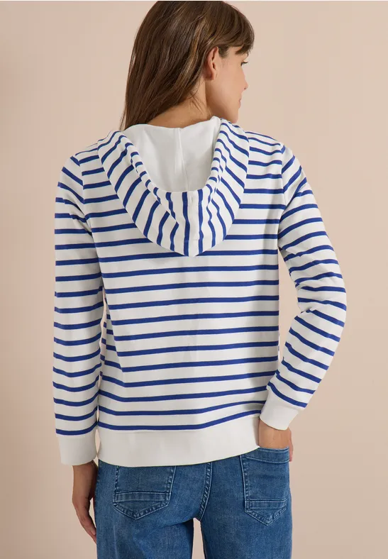 Vrouw van achteren in wit-blauw gestreepte hoodie en jeans.