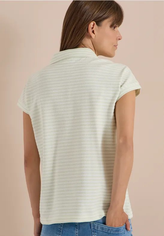 Femme de dos portant un polo à rayures blanc et vert clair à manches courtes.
