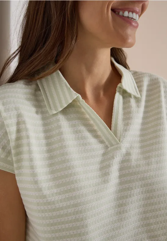 Gros plan sur une femme souriante portant un polo à col chemise rayé.