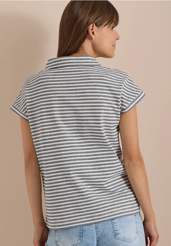 Frau steht seitlich, Rücken zur Kamera, trägt gestreiftes Kurzarmshirt und helle Jeans.