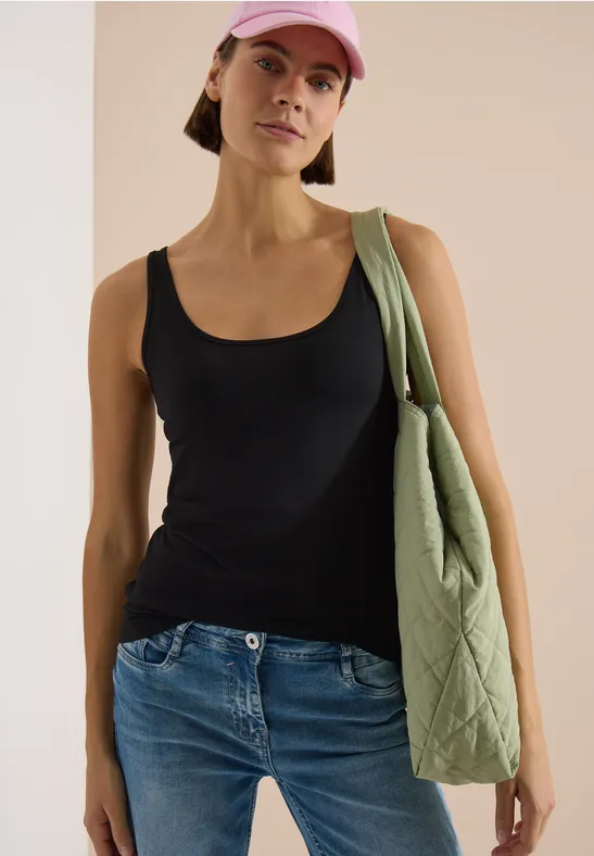 Femme en top noir et jean, avec un sac vert matelassé porté à l'épaule et une casquette rose.