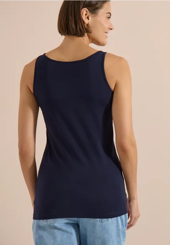 Femme de dos portant un débardeur bleu marine et un jean sur fond neutre.