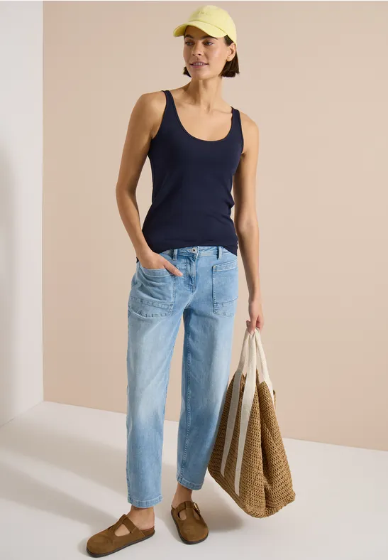 Femme en débardeur bleu marine et jean clair, portant un grand sac tressé et des sandales marron.