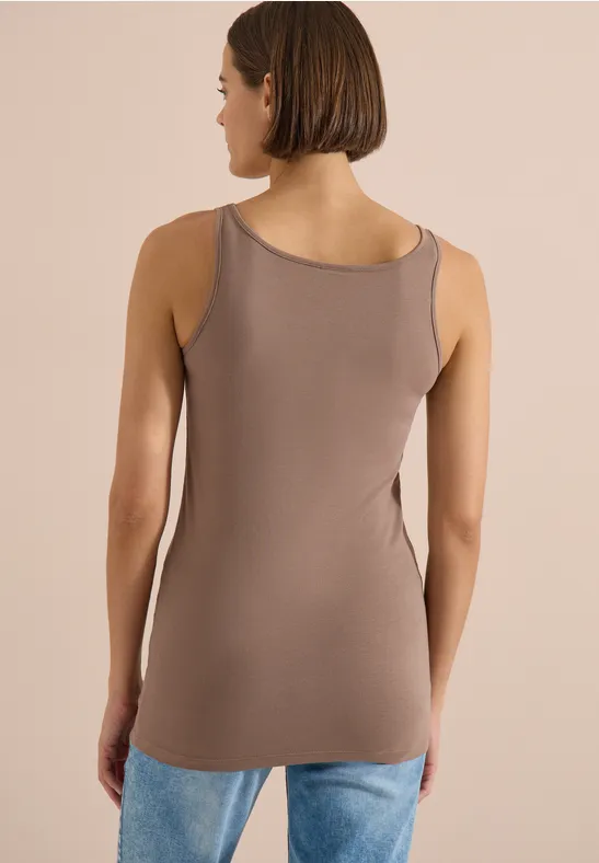 Vue de dos d'une femme portant un débardeur taupe et un jean devant un fond beige.