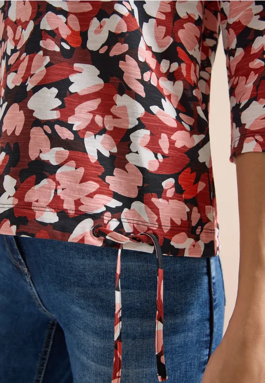 Rotes und weißes Blumenmuster auf schwarzem 3/4-Arm-Shirt kombiniert mit blauen Jeans.
