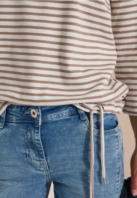 Haut beige à rayures blanches avec cordon de serrage sur le côté, associé à un jean bleu.