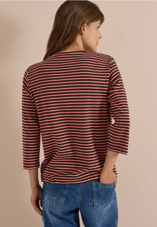 Silhouette de dos en tee-shirt rouille à rayures noires (manches 3/4) et jean bleu sur fond beige.