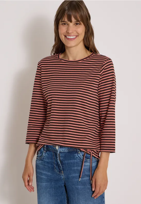 Jeune femme souriante en t-shirt à rayures et jean, posant devant un fond neutre.