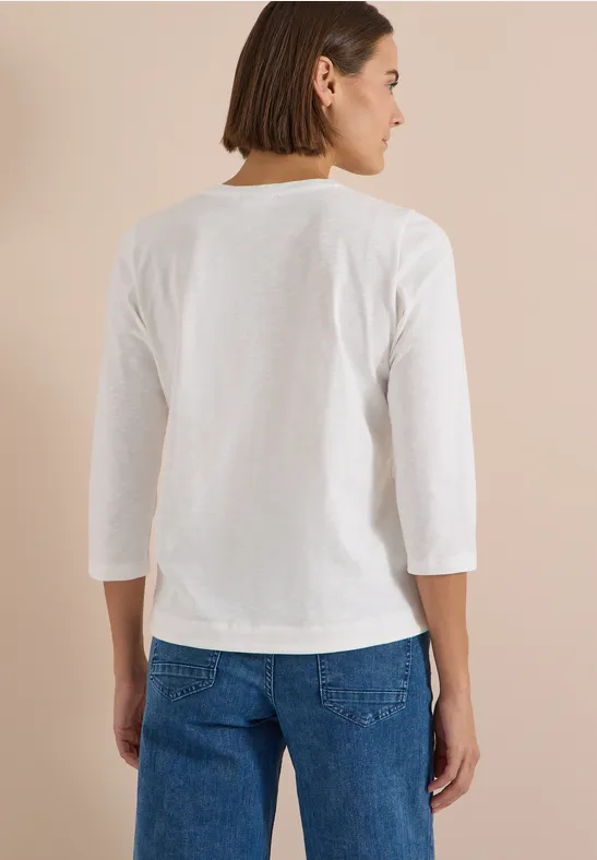 Femme de dos en t-shirt blanc à manches 3/4 et jean, fond beige.